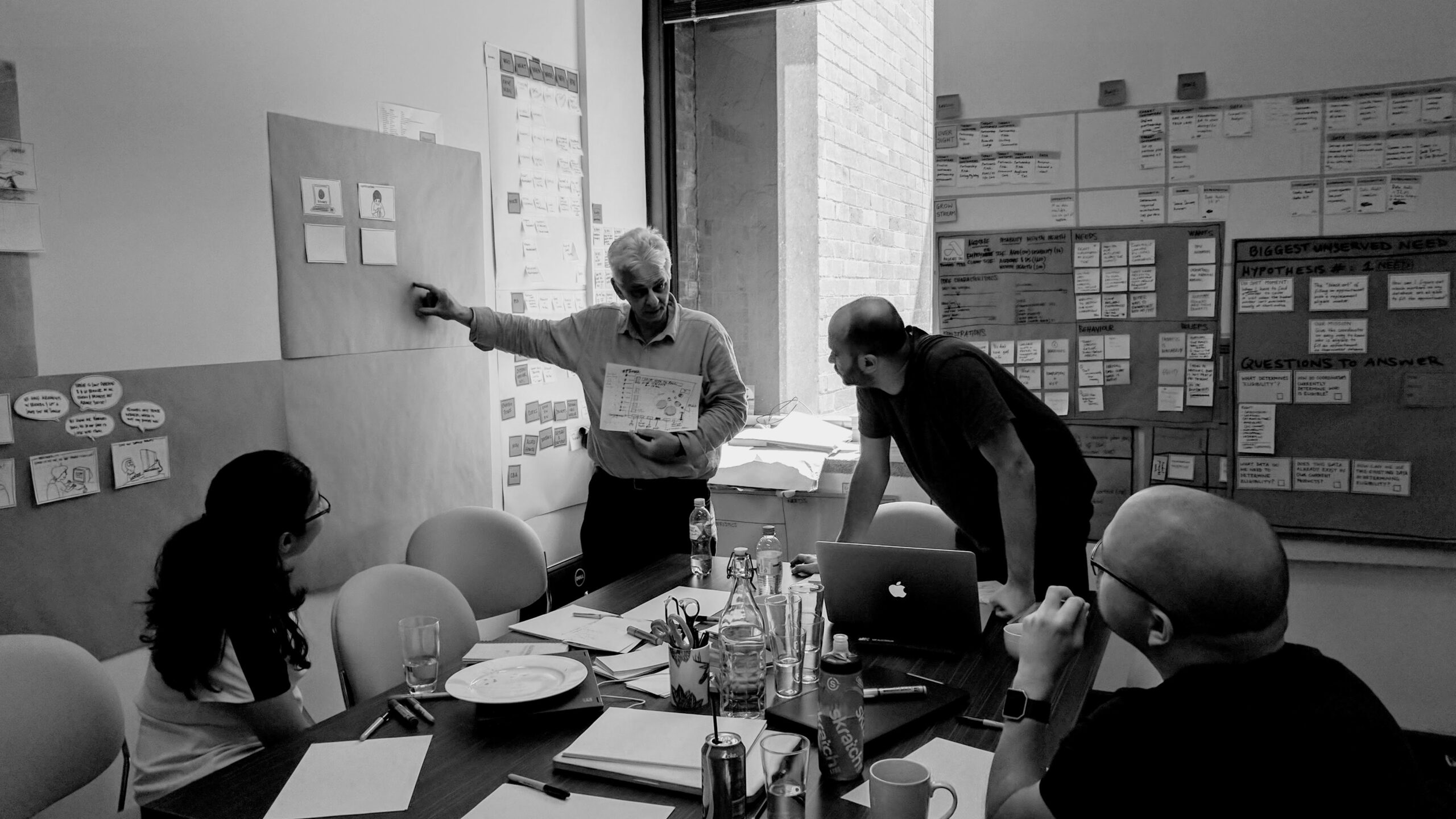 Team analyzing insights on a wall covered with notes and diagrams, collaboratively designing solutions to improve aged and disability care services.